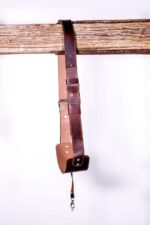 ull-length view of the Garioch single camera strap in dark brown leather, hanging on a wooden rail.