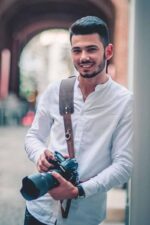 Man holding a camera with the Garioch single strap in dark brown leather worn crossbody.