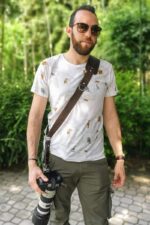 Man wearing the Garioch single camera strap in dark brown leather across the chest outdoors.