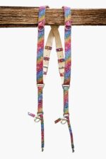 Rainbow multicolor leather dual camera harness with mosaic-textured snakeskin pattern, featuring natural vegetable-tanned leather padding, silver metal buckles, D-rings, and swivel snap hooks, hanging from a rustic wooden beam against a white background