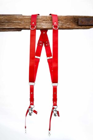 Red Campari leather camera harness front view showing shoulder straps draped over weathered wood bar, highlighting adjustable leather segments with metal connectors and center X-strap design