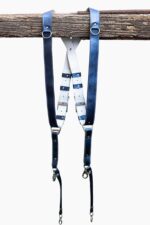 Royal Blue Metallic leather camera harness displayed flat on weathered wood showing full X-design with bright blue shoulder straps and white center strap with black and blue leather accent patches