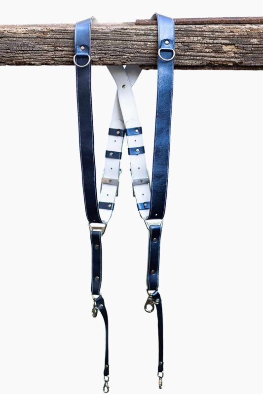 Royal Blue Metallic leather camera harness displayed flat on weathered wood showing full X-design with bright blue shoulder straps and white center strap with black and blue leather accent patches