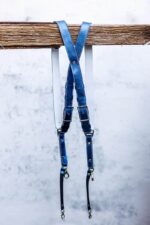 Royal Blue Metallic leather camera harness displayed on weathered wood beam, showing complete X-harness design with adjustable leather segments and metal D-ring attachments