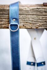 Royal Blue Metallic leather camera harness displayed on weathered wood beam, showing complete X-harness design with adjustable leather segments and metal D-ring attachments