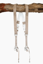 Sand-colored vintage leather dual camera harness with silver hardware, hanging from a rustic wooden branch against a white background, showing the full front view with two shoulder straps, a white leather back panel, branded "GENUINESTRAP" metal connectors, and snap hook attachments at each end.