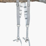 Silver glitter leather dual camera harness hanging from a rustic wooden branch against a light background, showing the full front view with two sparkle-finish shoulder straps, white leather back panel, D-rings, metal connectors, snap shackle clips, and lobster claw clasps at each end.