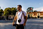 Photographer wearing a camera harness with third body extenders, walking outdoors with camera attached