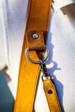 Close-up of tan leather camera harness extender attached to a D-ring with metal clasp