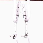 White leather dual camera harness hanging from a rustic wooden beam with adjustable straps and silver metal clips.