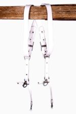 White leather dual camera harness hanging from a rustic wooden beam with adjustable straps and silver metal clips.