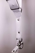 Close-up of a white leather camera harness connector with silver hardware and clasp detail.