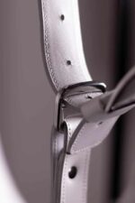 Close-up of a white leather strap adjustment point with punched holes and silver metal buckle.