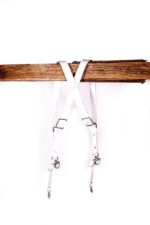 Back view of a white leather dual camera harness hanging from a wooden beam with crossed straps.