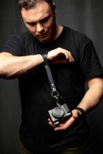 Man wearing the black leather camera wrist strap on his wrist, adjusting it in a studio setting