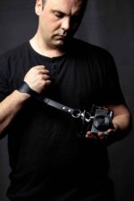 Man wearing the black leather camera wrist strap while holding a camera, studio lifestyle shot.