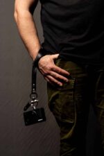 Man wearing the black leather camera wrist strap, holding a camera at his side.