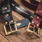 Close-up of black and burgundy belts with brass buckles on wood