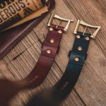 Two leather belts on wooden surface with brass buckles (burgundy and navy)