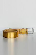 Gold padded leather trouser belt partially unrolled on light background, front view of the buckle