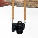 Third body camera harness extender straps in tan leather holding a DSLR camera on white background