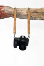 Third body camera harness extender straps in tan leather holding a DSLR camera on white background