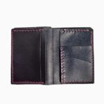Interior view of a black leather bifold wallet opened flat and empty, showing two card pockets on the left side and two angled card slots on the right side, all finished with fuchsia pink hand-stitching, against a white background.