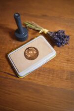 Custom wood stamp ink pad with engraved wooden lid beside a stamp handle and dried lavender on a wooden tabletop.