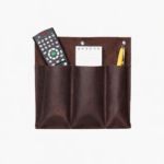 Dark brown leather double wall pocket organizer holding remote controls, notepad, and pencil on a light background.