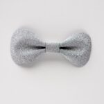Close-up of a single silver glitter leather bow tie on a clean white background, showing the textured sparkle finish and sculpted butterfly shape.