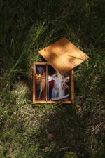 Open wooden photo box lying in the grass with printed photos, dried lavender, and a ribbon inside