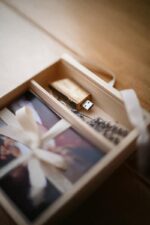 Close-up of a wooden keepsake box containing a USB drive, photo prints, ribbon, and dried lavender