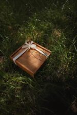 Closed wooden box tied with a cream ribbon resting in tall grass