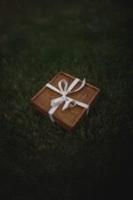 Wooden keepsake box wrapped with a white ribbon sitting on dark green grass