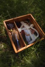 Open wooden box in the grass with photo prints, a ribbon, dried lavender, and a small glass vial