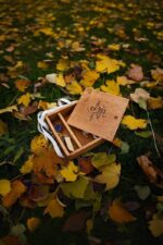 Open wooden memory box placed on autumn leaves with compartments for photos and a USB drive