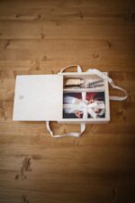 Light wooden photo box on a wooden table with printed photos, a ribbon, dried lavender, and a USB drive