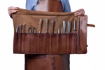 Chef holding the knife holder professional 11s rolled and buckled shut, front view showing dual brass buckle straps