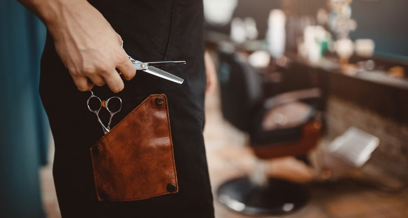 Barber holding professional scissors with a leather tool holster in a barbershop