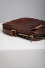 Close up of the brass zip on the brown leather reporter crossbody bag