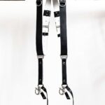 Black GenuineStrap SW Edition leather camera strap with white inner padding, showing D-ring ends hanging over wooden beam
