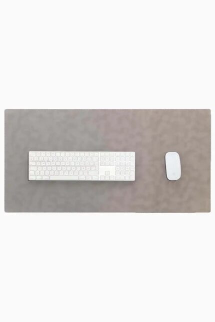 Top-down view of a light gray leather desk mat with stitched edges on a white background, with a white full-size wireless keyboard centered on the left and a white wireless mouse on the right.